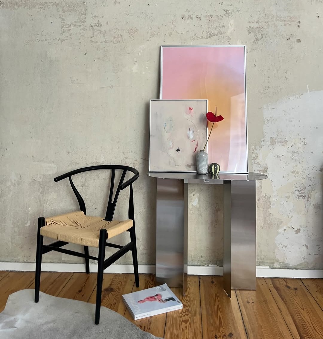 Minimalistische Wohnszene mit Stuhl, Metalltisch und blomus Vase mit roter Blume vor strukturierter Wand