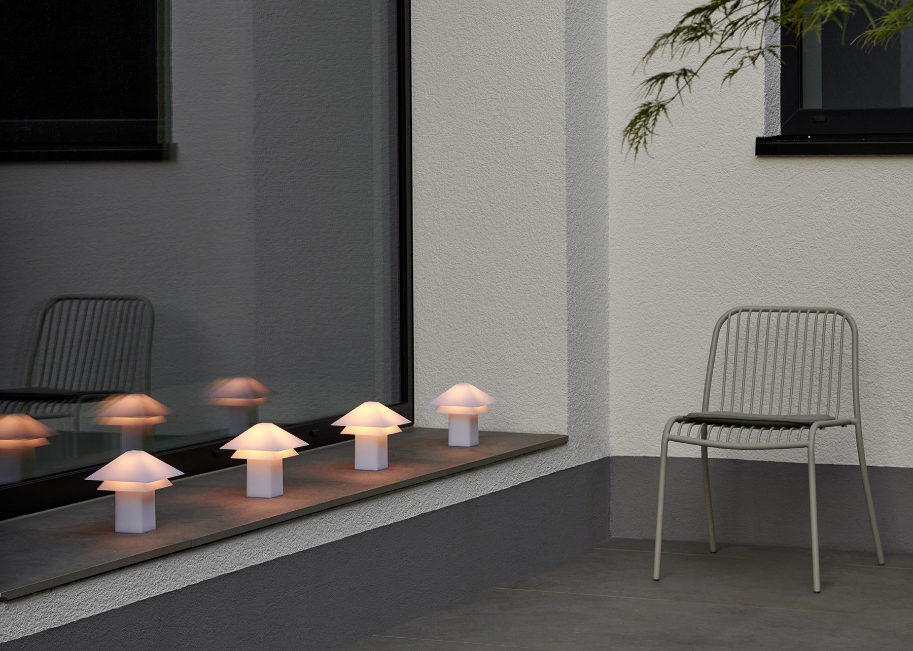 Cadre extérieur moderne avec des lampes champignons lumineuses et une chaise minimaliste près de la fenêtre.
